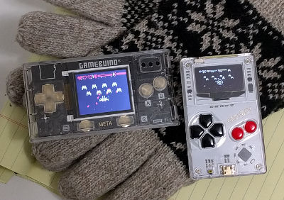 A Gamebuino META next to an Arduboy, both running an early build of Defend Pluto